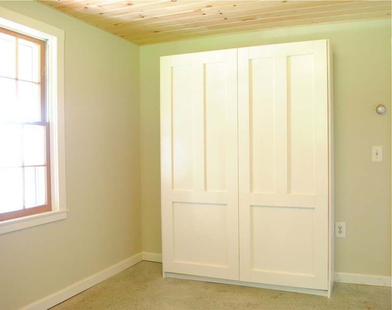 Folded wall-mounted Murphy bed in a bright studio apartment, finished in white paint.