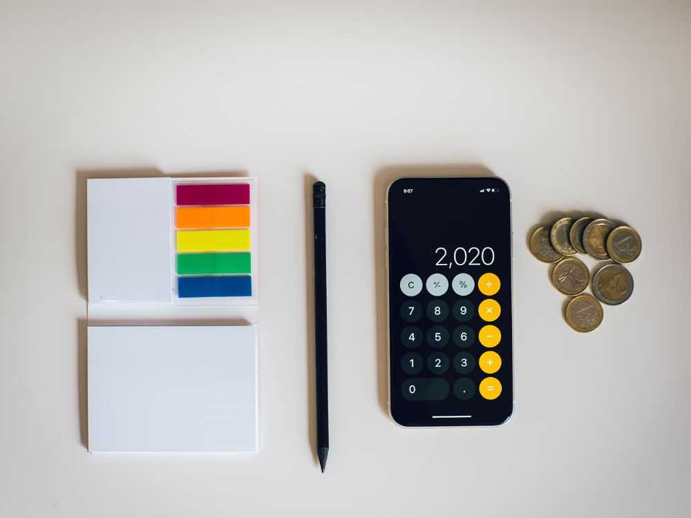An image of notepads, a pen, calculator app on a phone and coins. 