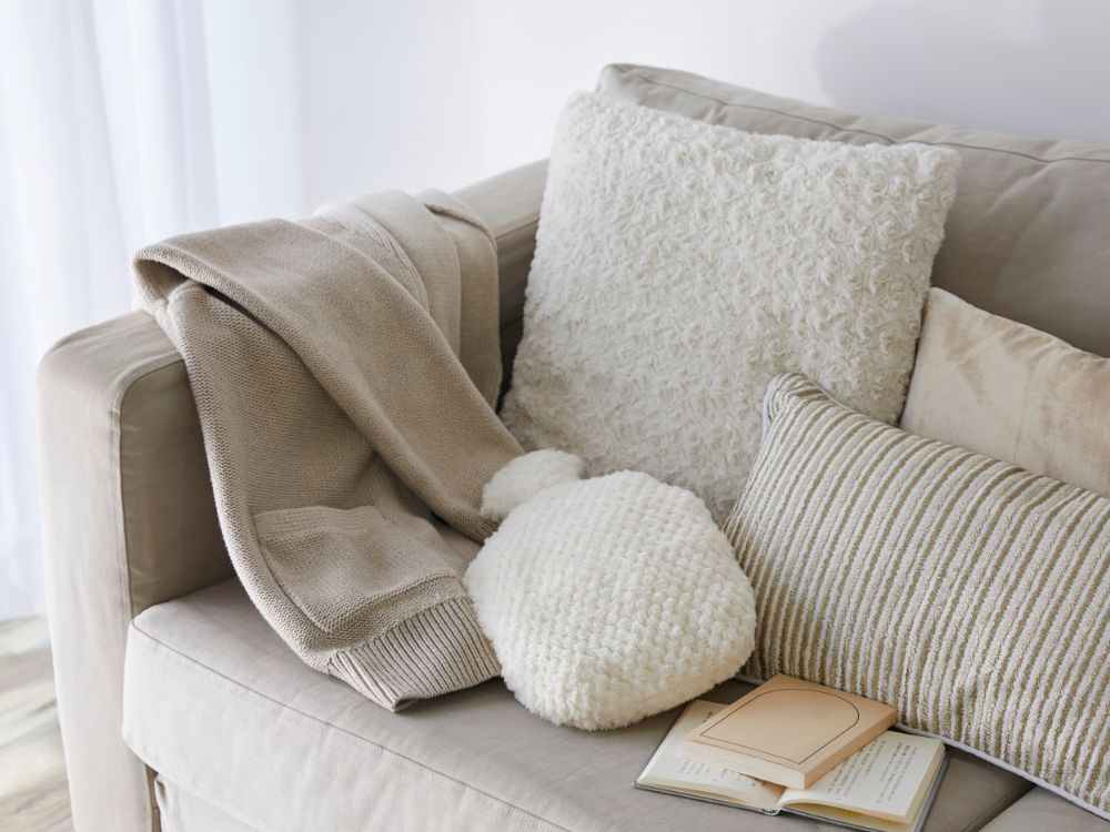 An image of a couch, throw pillows, and curtains with neutral color. 