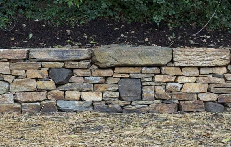 Building a dry stone retaining wall is well within your abilities. This is a great example of a retaining wall that does NOT interfere with the natural site drainage.